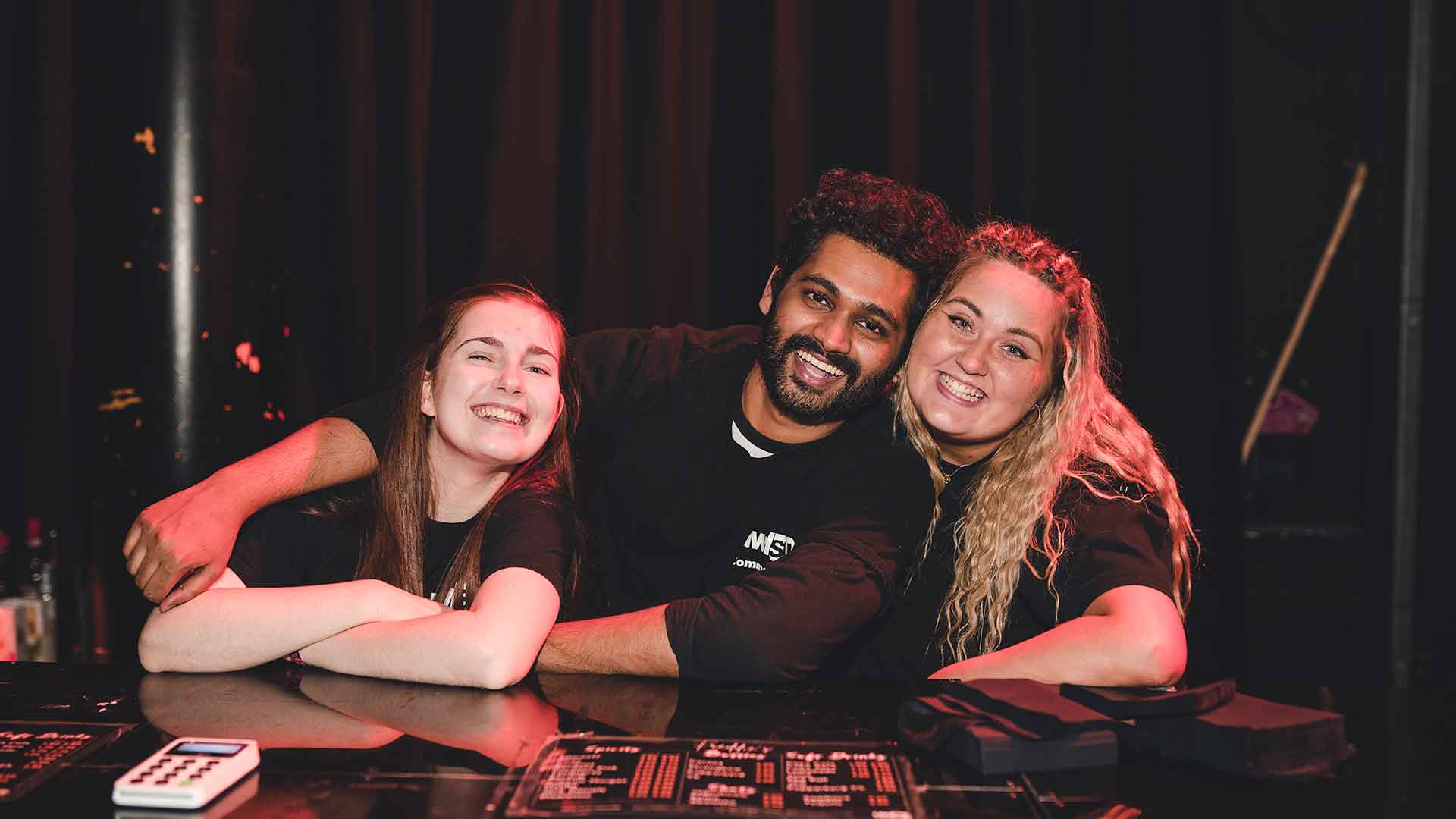 Three staff members laughing and smiling at the camera with their arms around each other