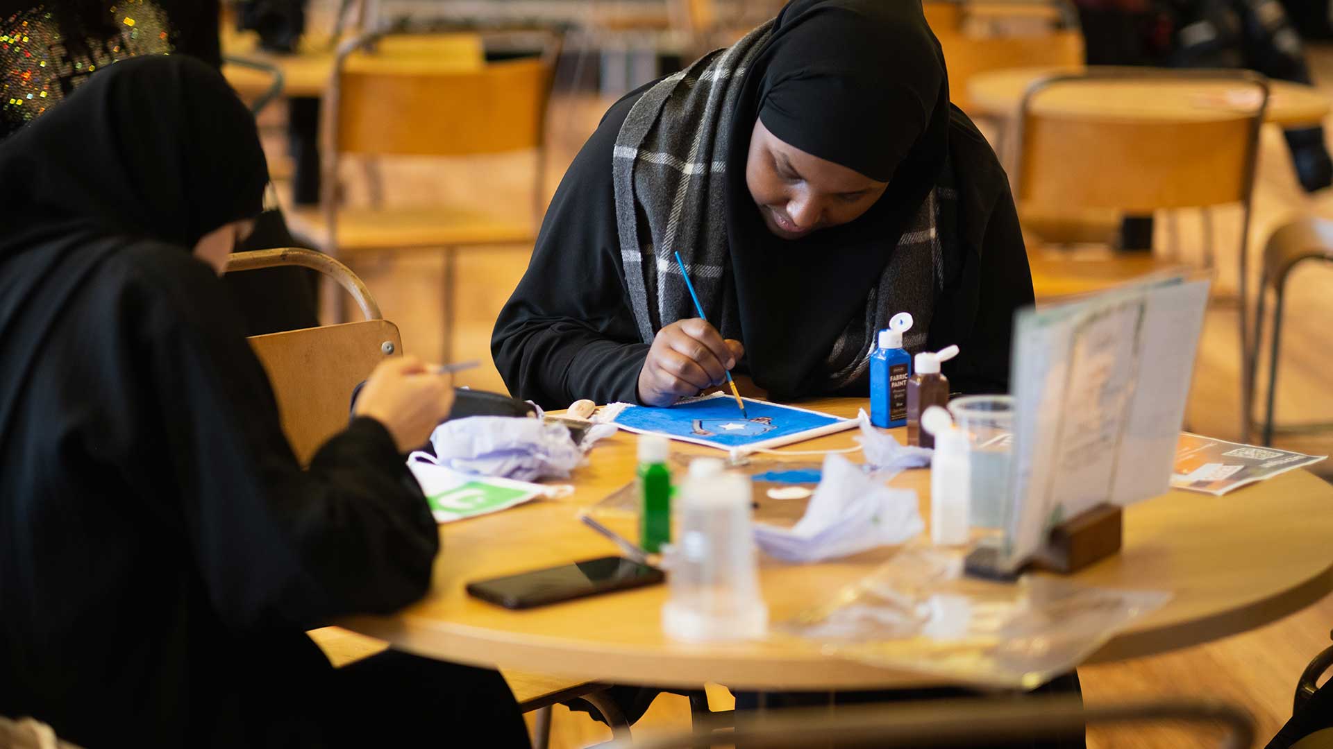 International students at a creative event, sat at a table painting